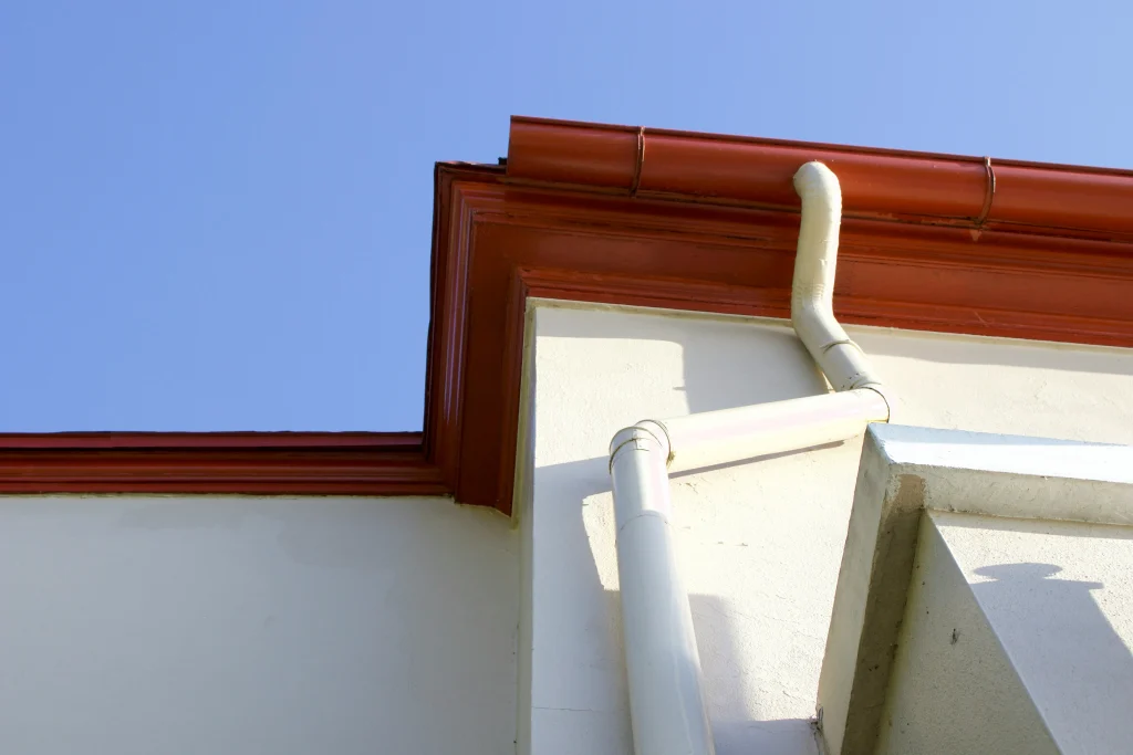Close-up of a red roofline and white PVC guttering system on a house in Worcester under a clear blue sky, showing well-maintained gutters and downpipes.